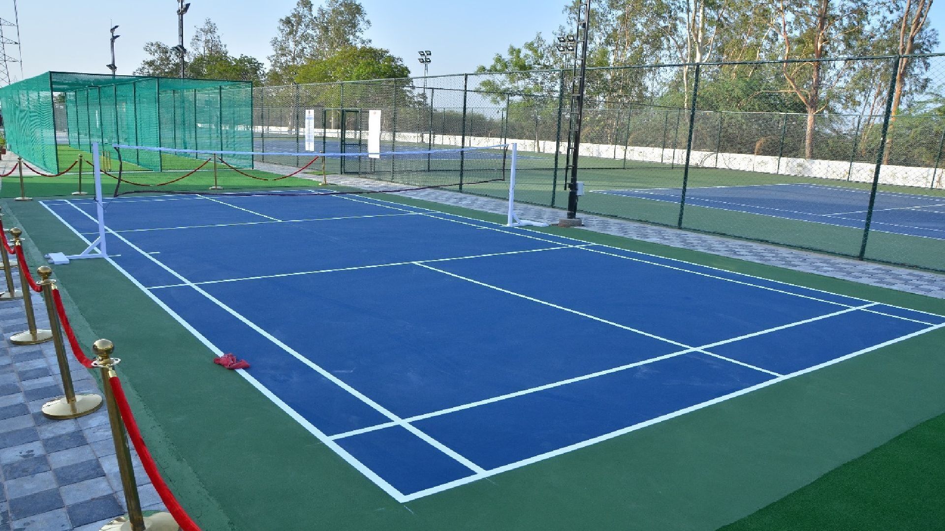 A tennis court with green and blue surfaces, surrounded by a fence and trees.