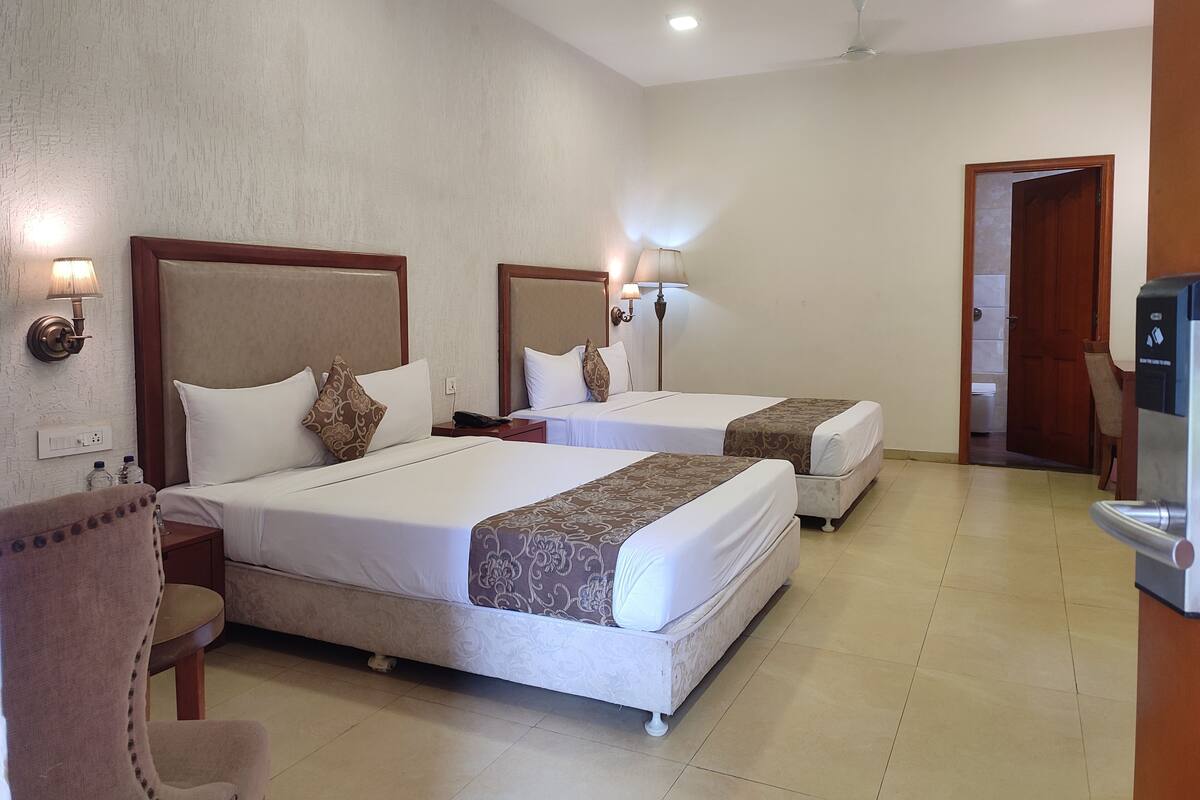 A hotel room with two beds, a desk, a chair, a TV, and a bathroom visible through an open door.