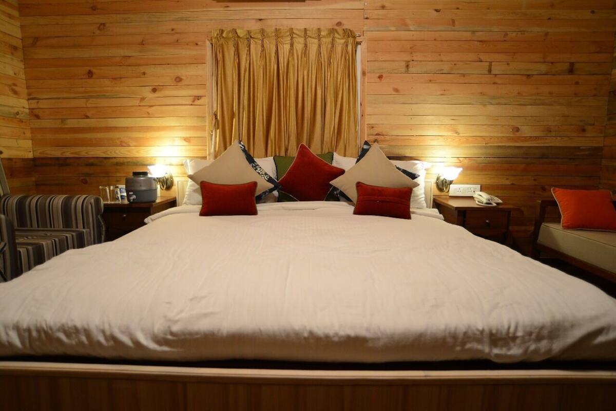 A wooden-paneled room with a large bed, two bedside tables, and a window with curtains.