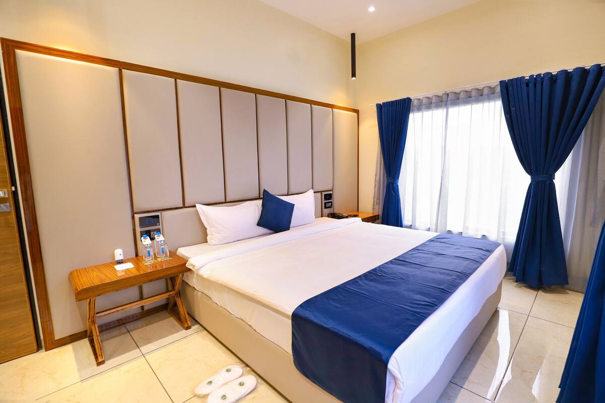 A hotel room with a large bed, a wooden nightstand, a bedside table, and a bathroom scale.
