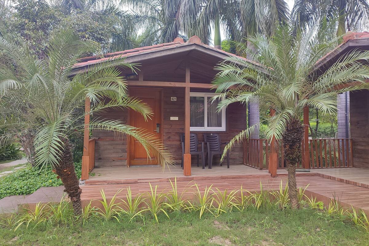 A wooden cabin with a tiled porch, a door with a number plate, and two chairs outside.