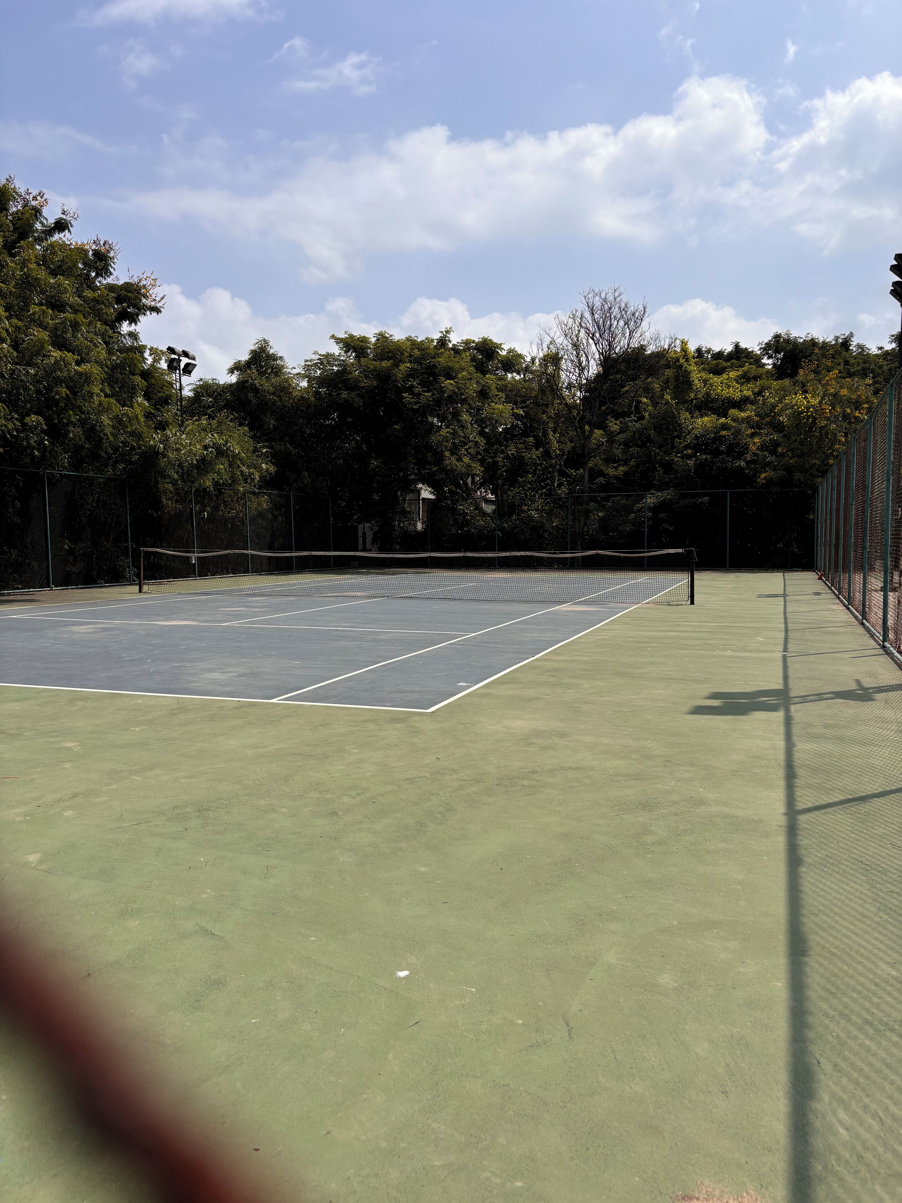 A tennis court with a net, surrounded by trees and a fence.