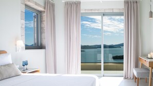 A bedroom with a large bed, a nightstand with glasses, a desk with a chair, and a view of the sea through a sliding door. - Elegant stone-built Villa, with heated pool and amazing view (Lefkada)