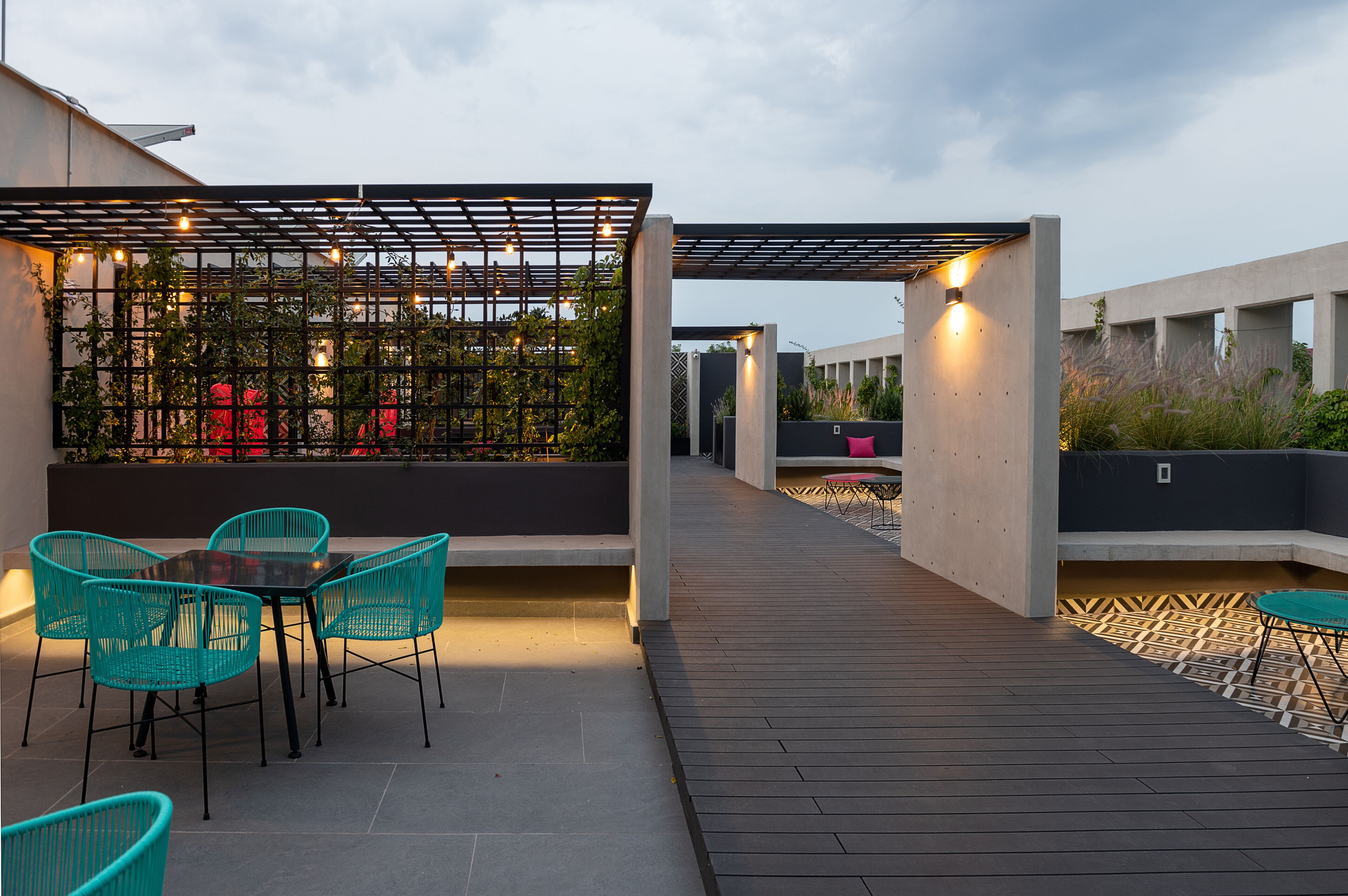 An outdoor patio with a wooden deck, a table with chairs, and a pergola with string lights.
