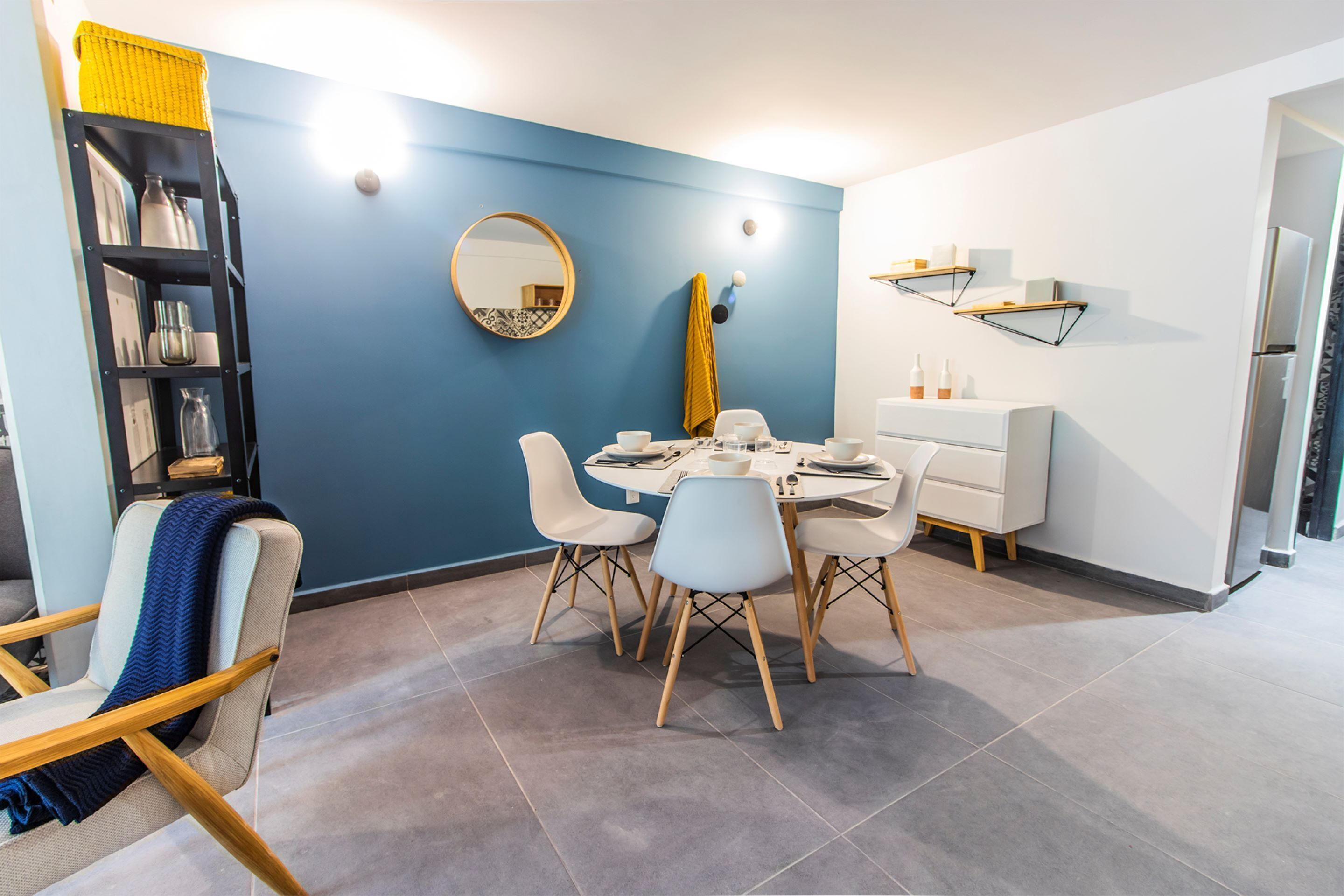 Un espace repas moderne avec une table ronde, des chaises blanches et un mur d’accent bleu.