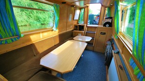 A compact train compartment with a wooden table, two cushioned seats, a small kitchenette, and large windows with curtains. - Floating Holidays (Stockport)