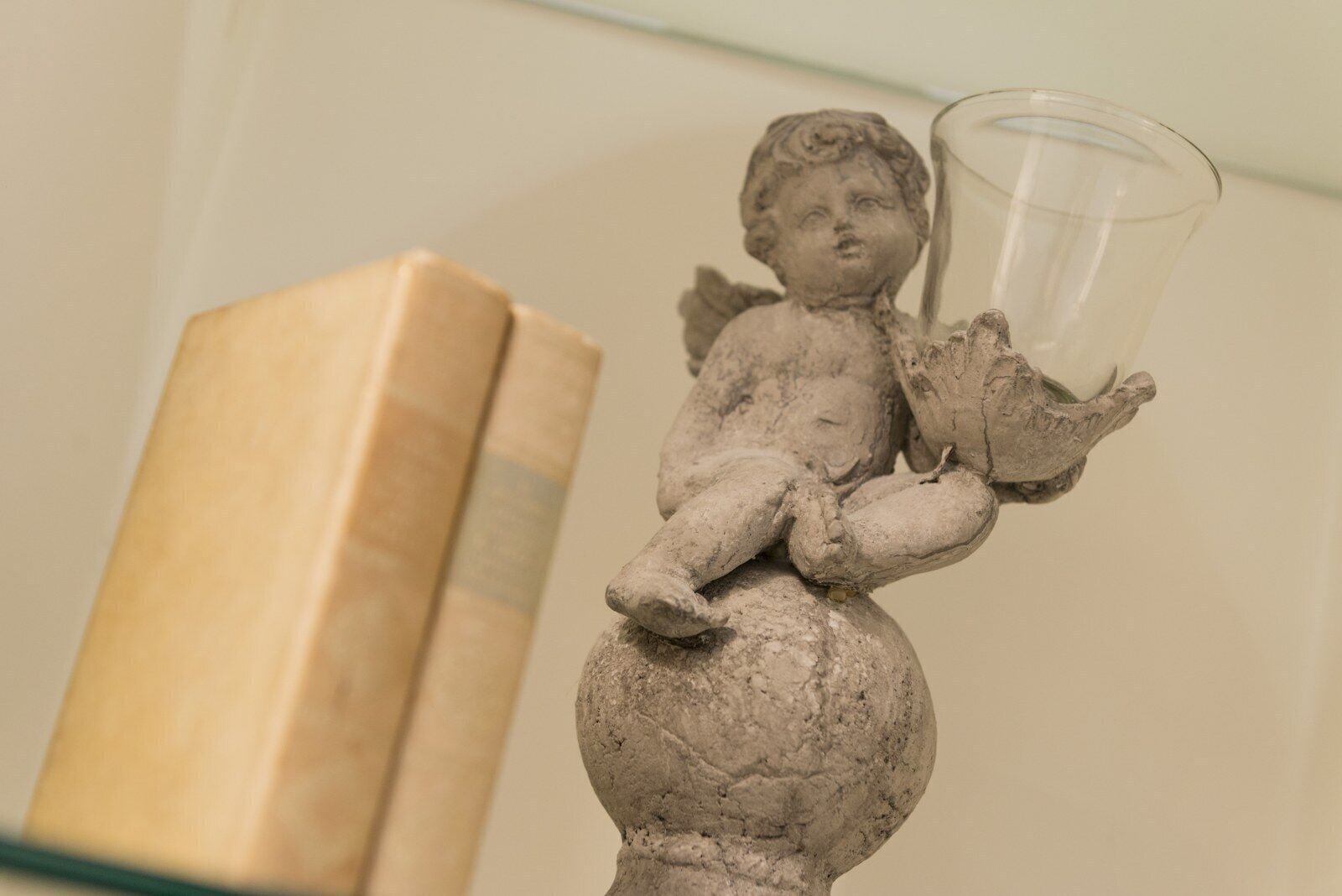 A statue of a cherub holding a glass, with a book in the background.
