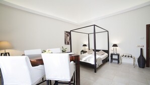 Una habitación de hotel moderna con una cama con dosel, una mesa de comedor con sillas, una mesita auxiliar pequeña, una lámpara y un jarrón.