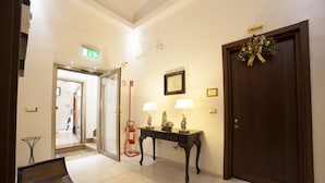 Un vestíbulo de hotel con mostrador de recepción, extintor, puerta decorada con un adorno y suelo estampado.