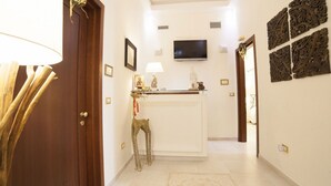 Un pasillo con una puerta de madera, un mostrador de recepción blanco, un televisor montado en la pared y decoración mural.
