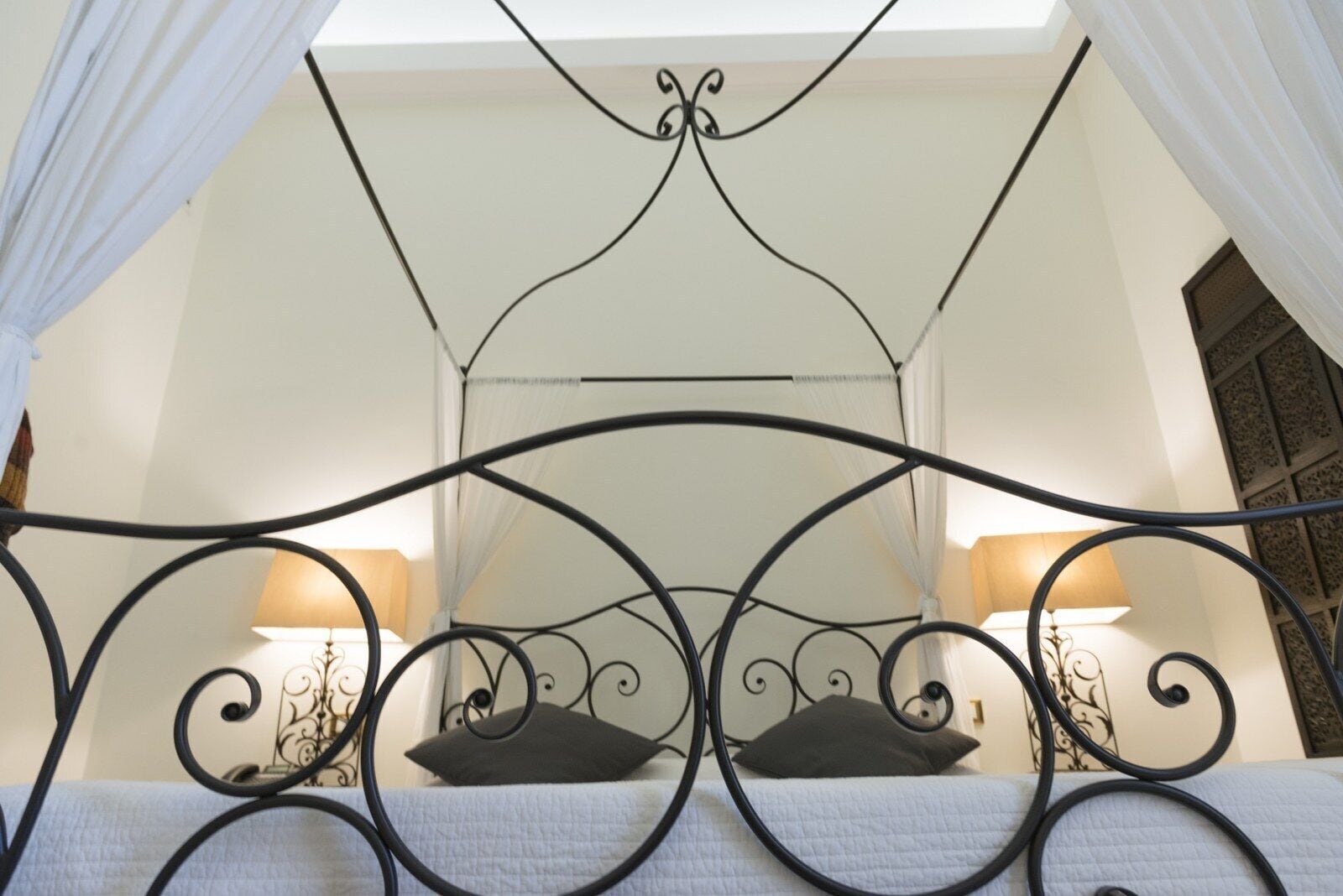 Ein Bett mit schwarzem Metallgestell, weißen Vorhängen und zwei Nachttischlampen.