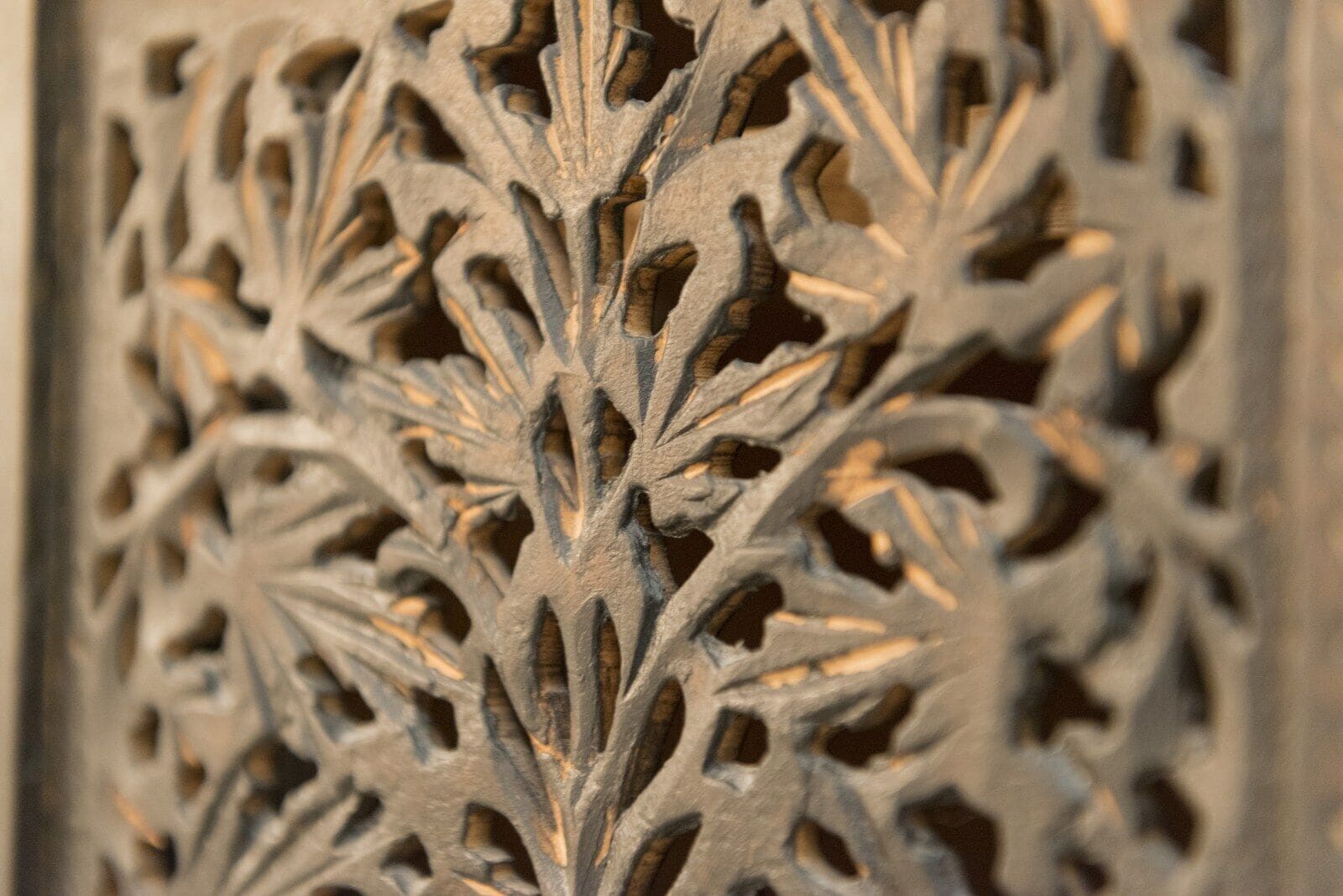A close-up of a detailed carved wooden panel with a symmetrical, leaf-like pattern.