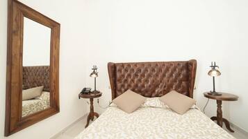 A bedroom with a tufted headboard, a large mirror, two bedside tables with lamps, and a patterned bedspread.