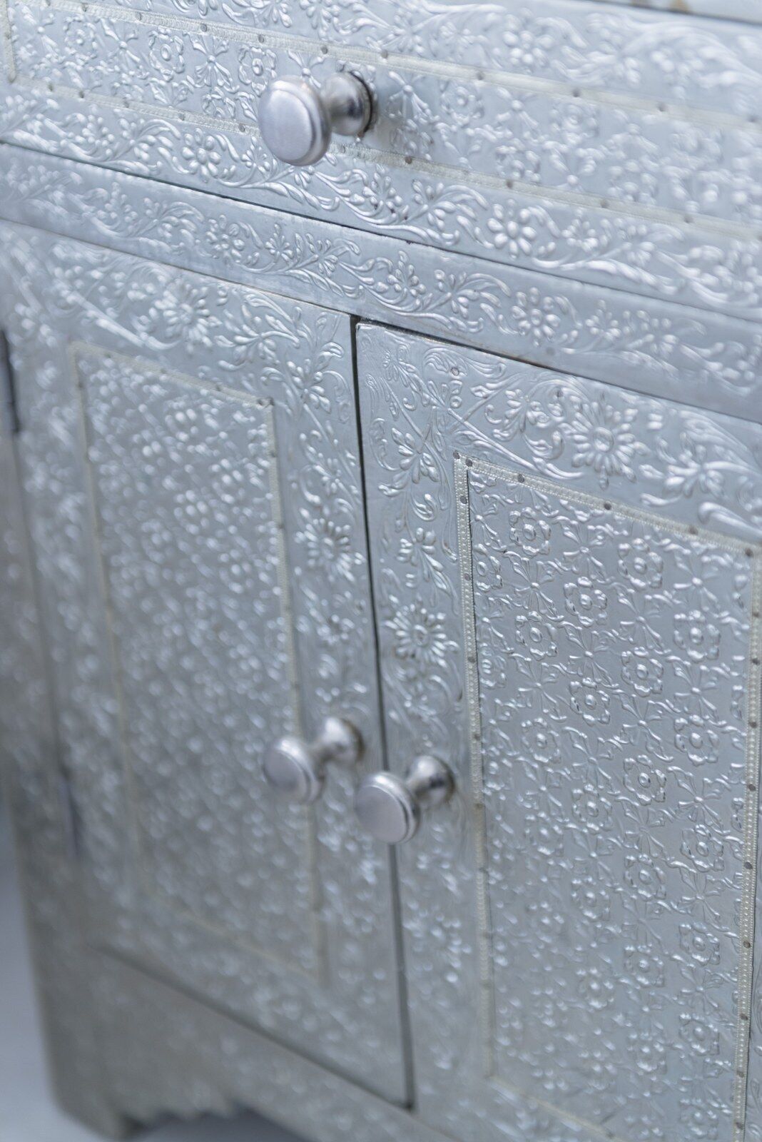 A metallic cabinet with intricate floral patterns and two round knobs.