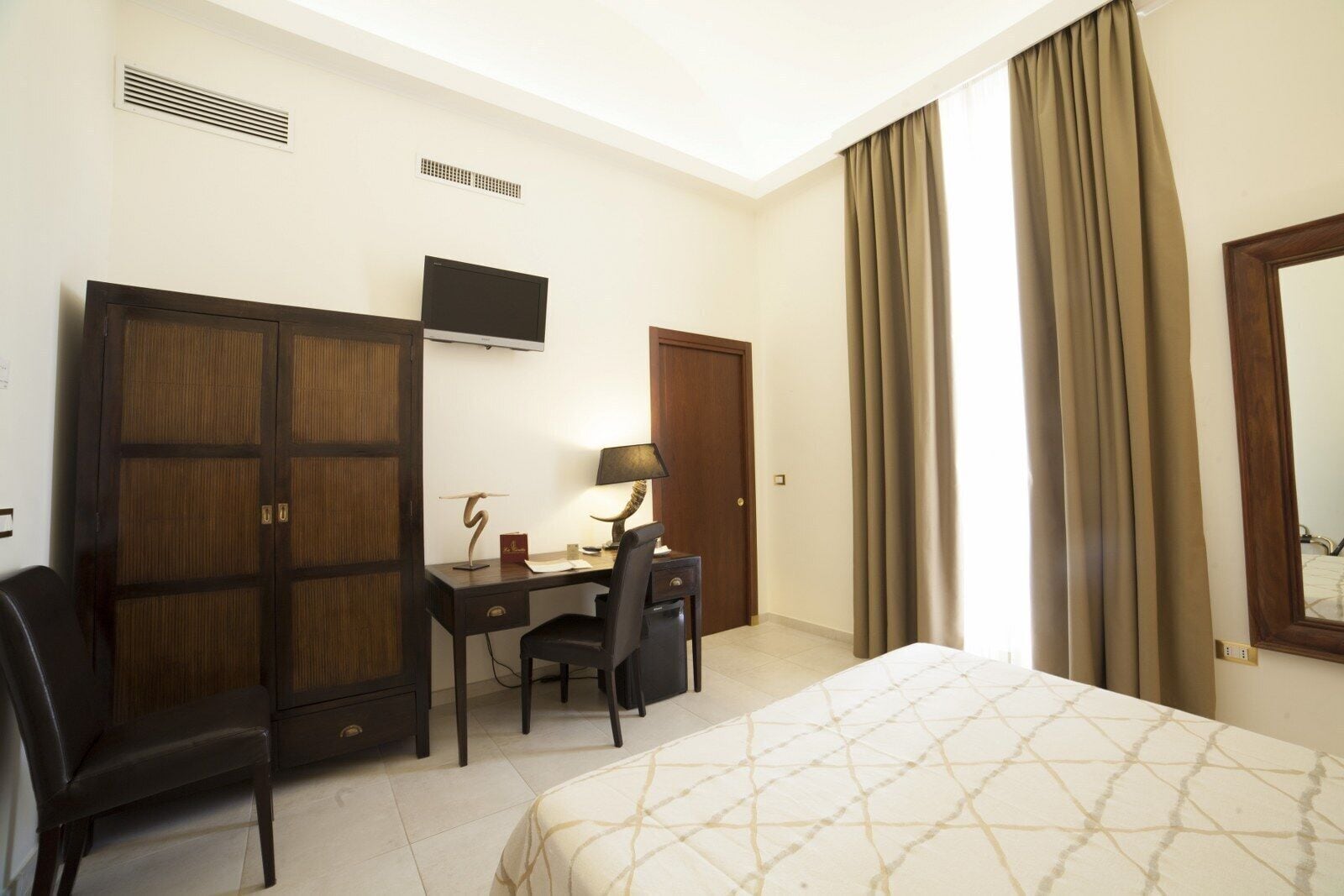 Una habitación de hotel con cama, escritorio, silla, televisor y armario.
