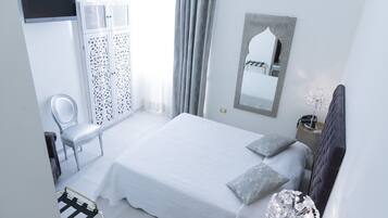 Un dormitorio con cama, una silla, armario, espejo y mesita de noche.