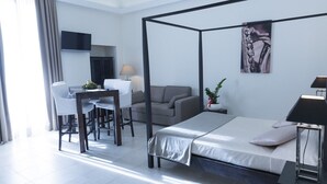 Una habitación de hotel moderna con una cama con dosel, un escritorio con silla, un sofá, un televisor y una lámpara.