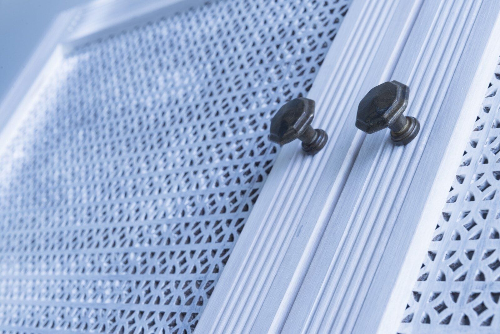 A close-up of a window with a metal mesh screen and two brass knobs.