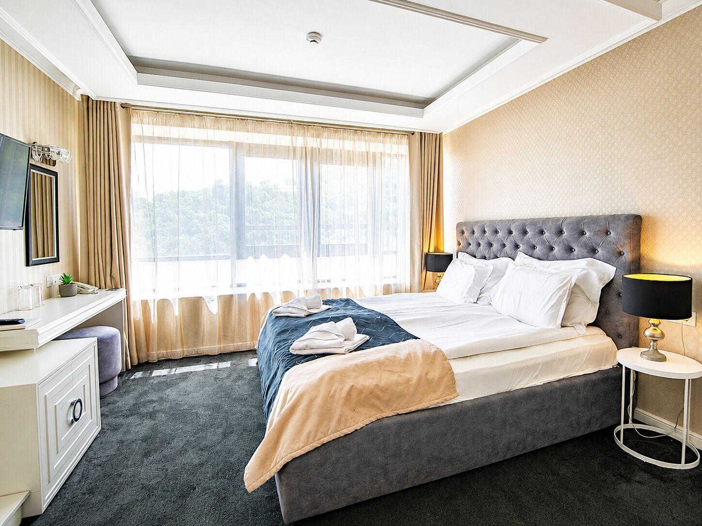 Une chambre d’hôtel avec un lit, une table de chevet, une lampe et une vue sur la verdure par la fenêtre.