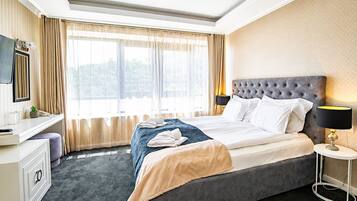 Habitación de hotel con cama, mesita de noche, lámpara y vista a zonas verdes a través de la ventana.