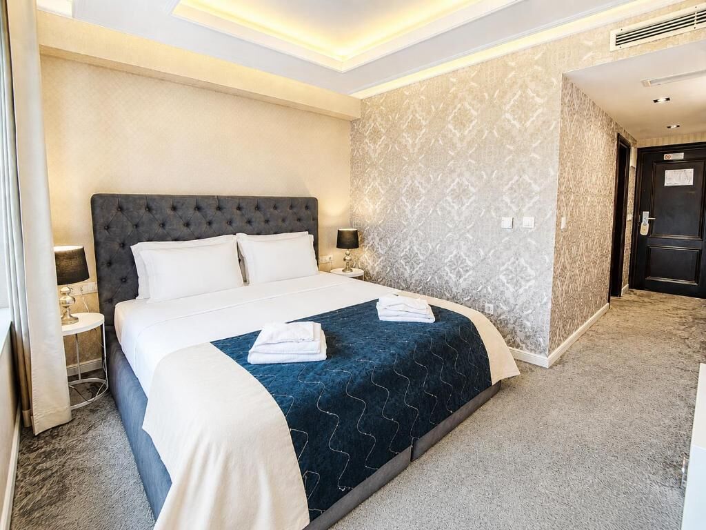 A hotel room with a large bed, a nightstand, a lamp, and a door.