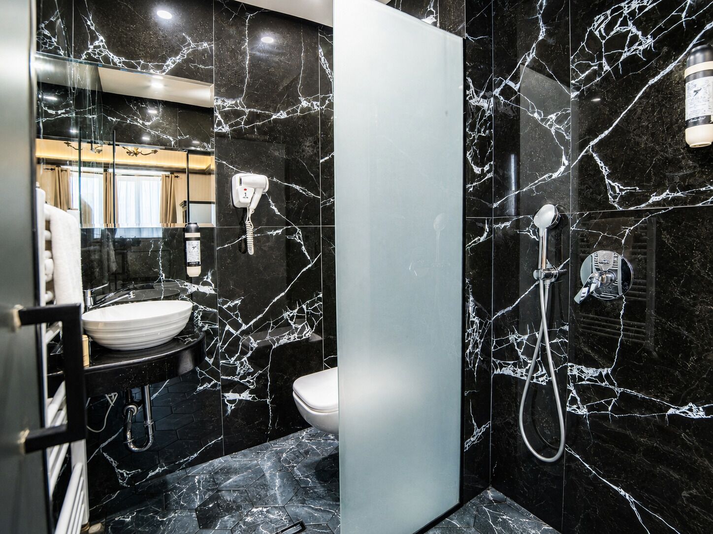 A bathroom with a black marble sink, a toilet, and a shower area.