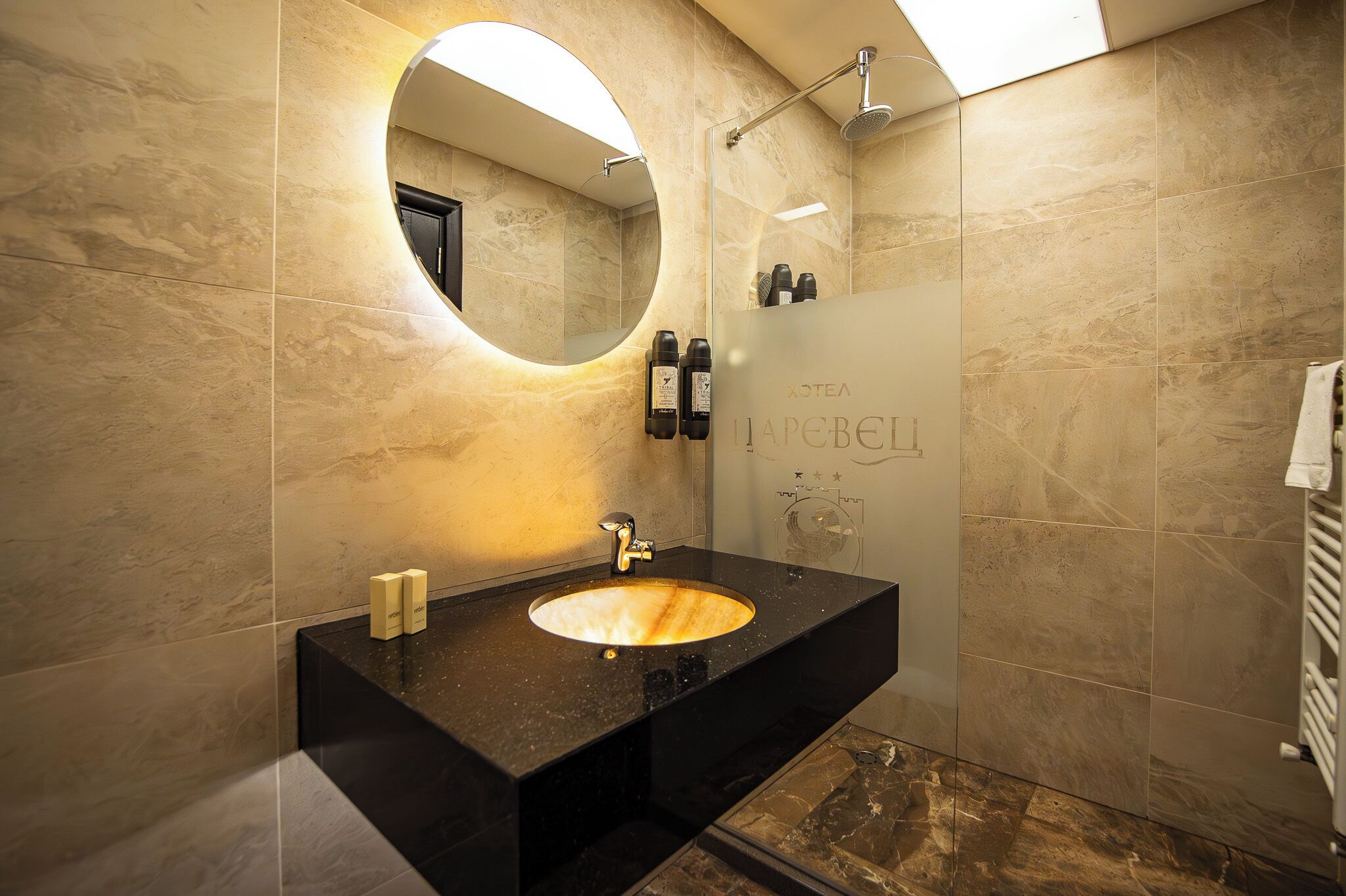 A modern bathroom with a round mirror, a sink, and a glass shower enclosure.