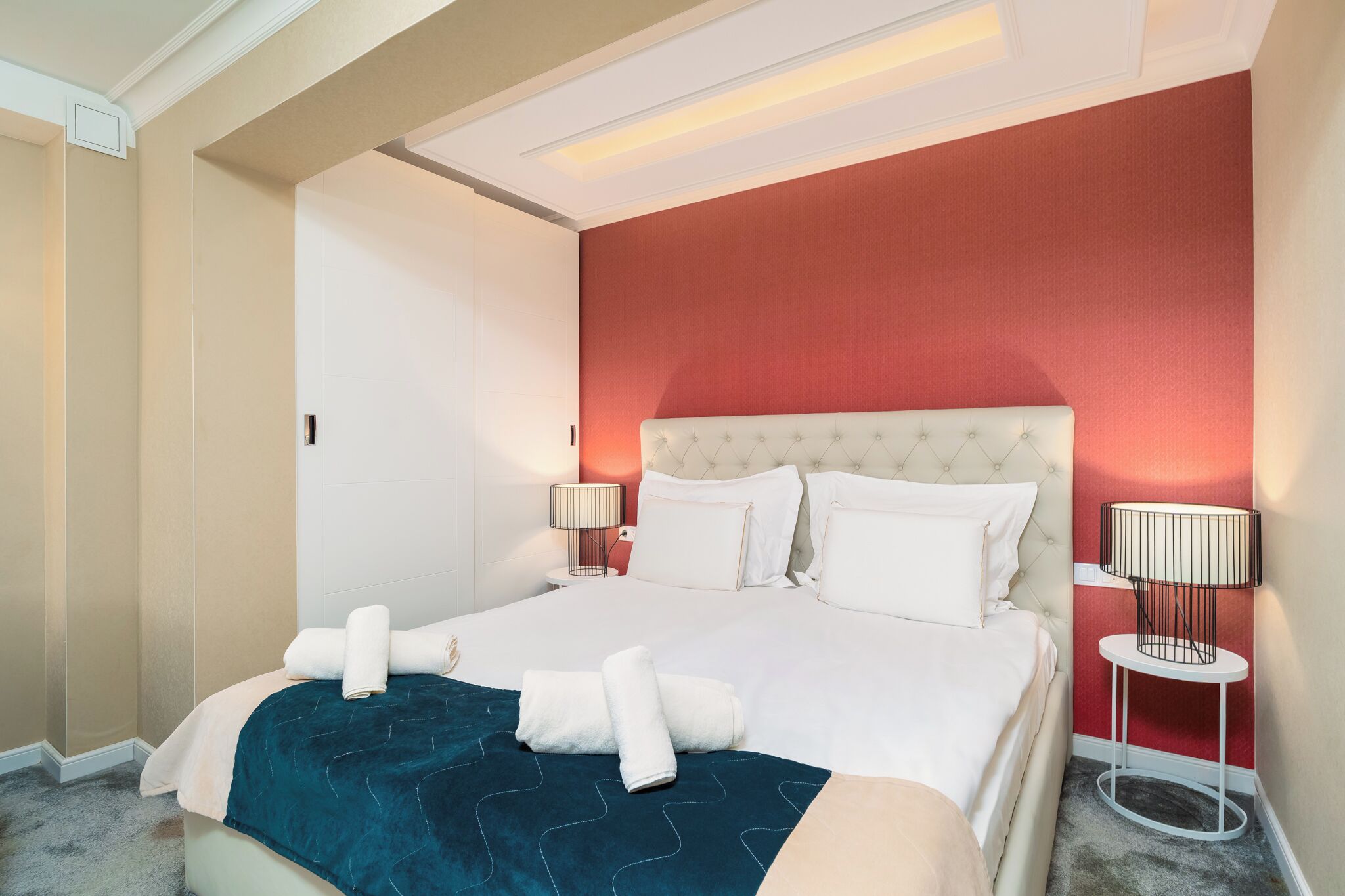 Une chambre d’hôtel avec un lit, deux tables de chevet, un mur d’accent rouge et un luminaire au plafond.