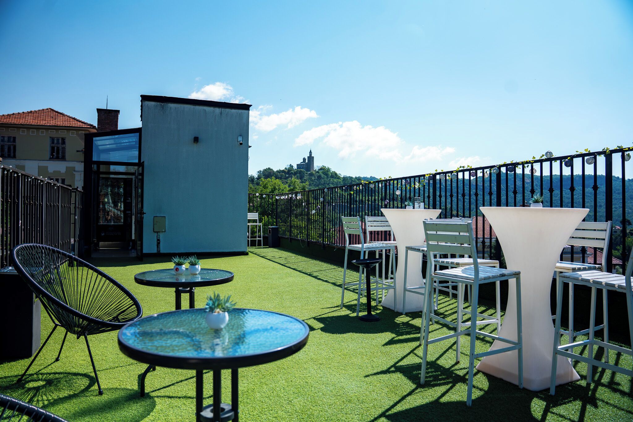 Terraza en la azotea con mobiliario exterior, un edificio pequeño y una vista a un castillo distante.