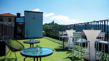 Terraza en la azotea con mobiliario exterior, un edificio pequeño y una vista a un castillo distante.