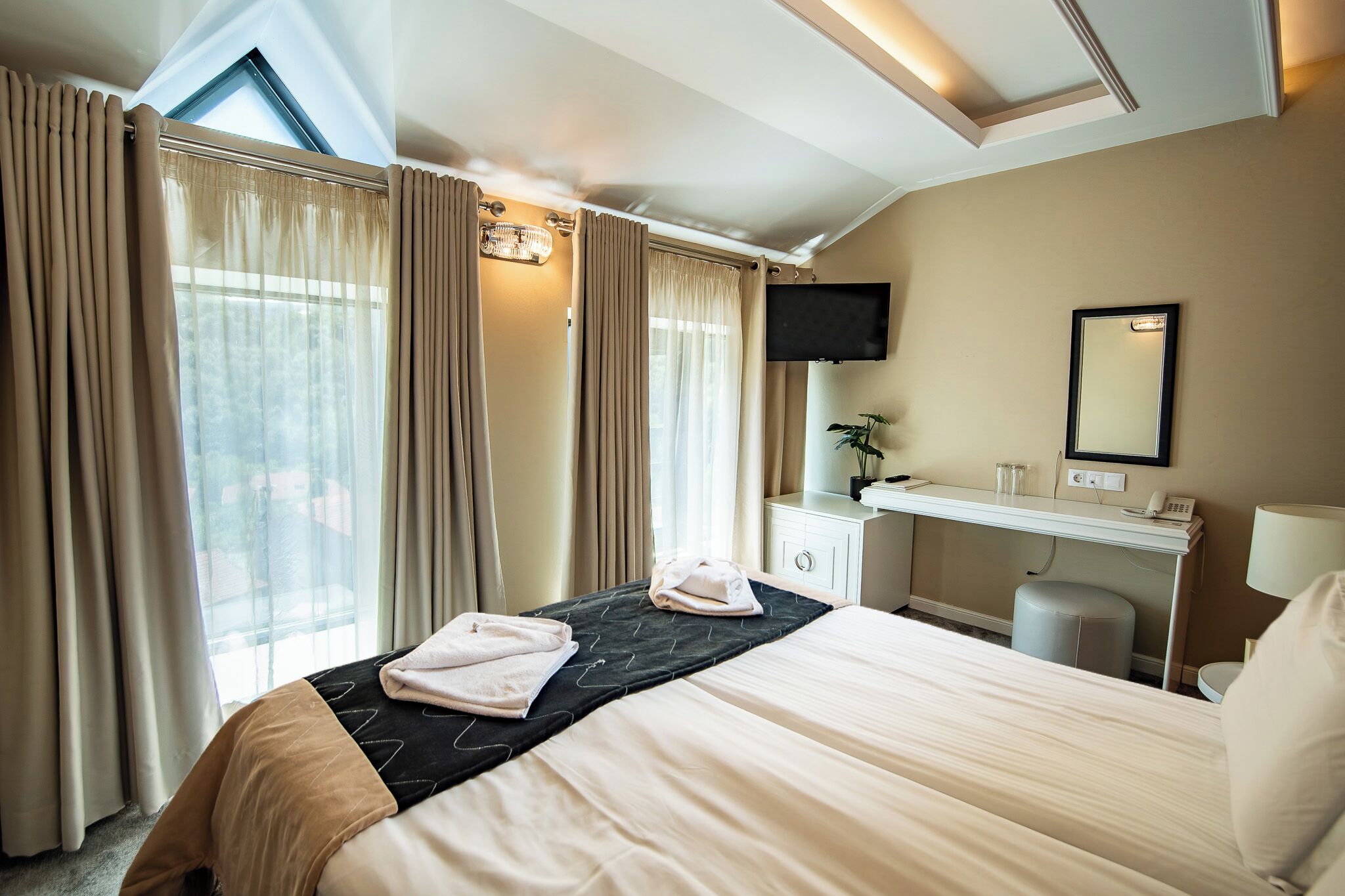 A hotel room with a bed, a desk, a chair, a TV, and a window with curtains.