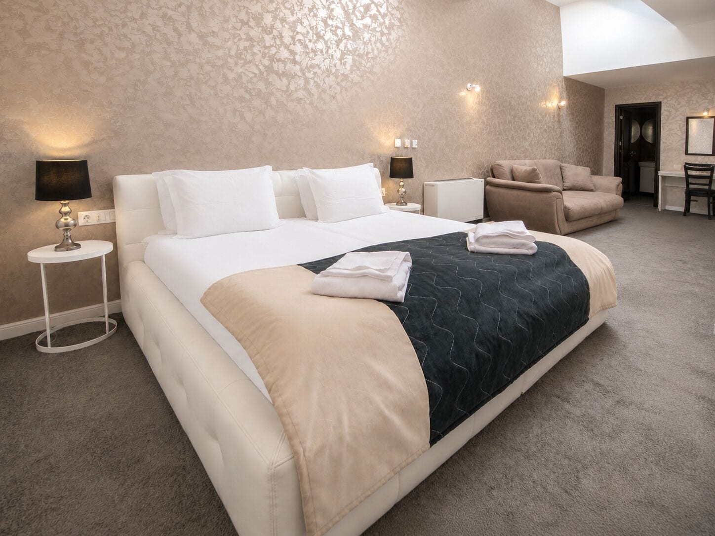 A hotel room with a large bed, a sofa, a small table, and a chair.