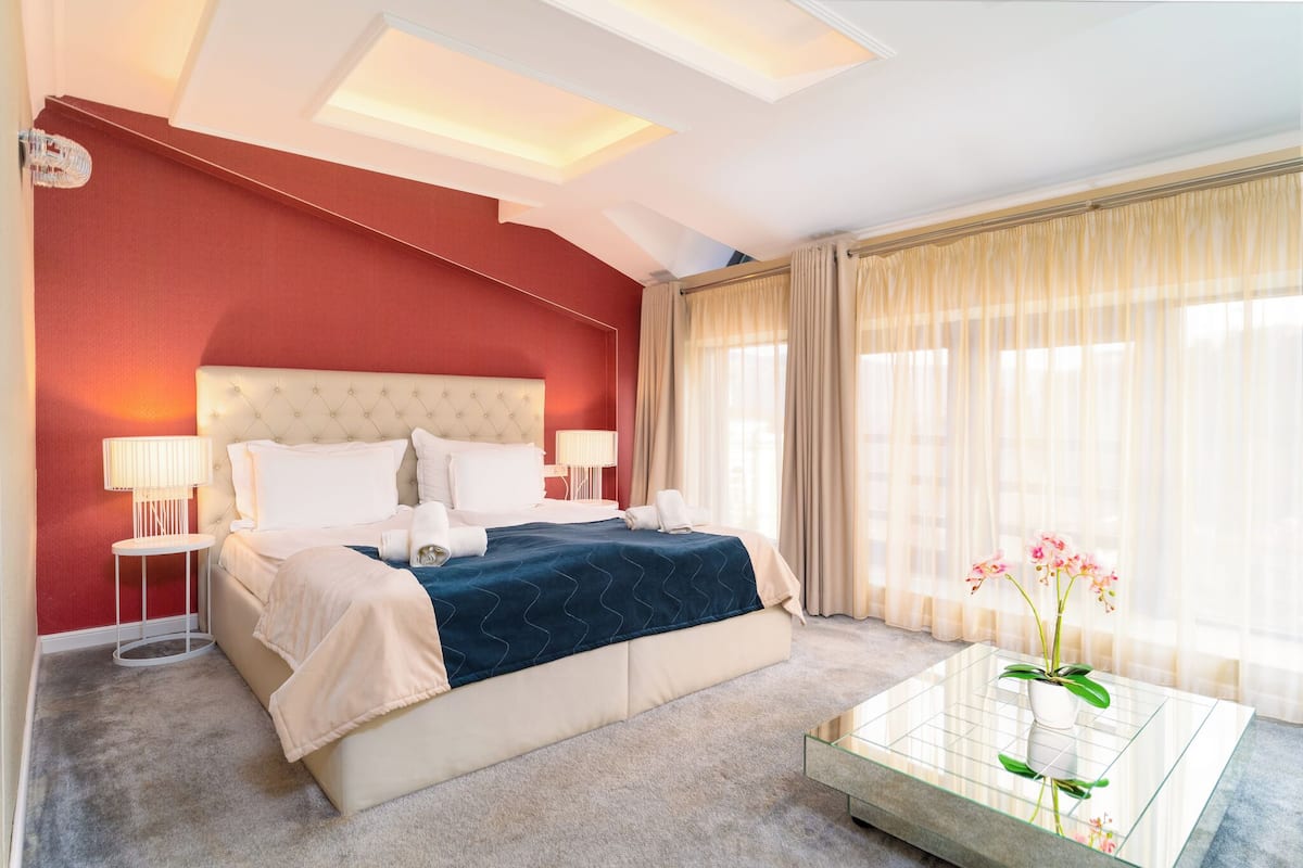 A hotel room with a large bed, bedside lamps, a glass coffee table, and a view of the outdoors.