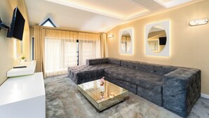 Een moderne woonkamer met een modulaire bank, een glazen salontafel, een flatscreen televisie en een groot raam met gordijnen.