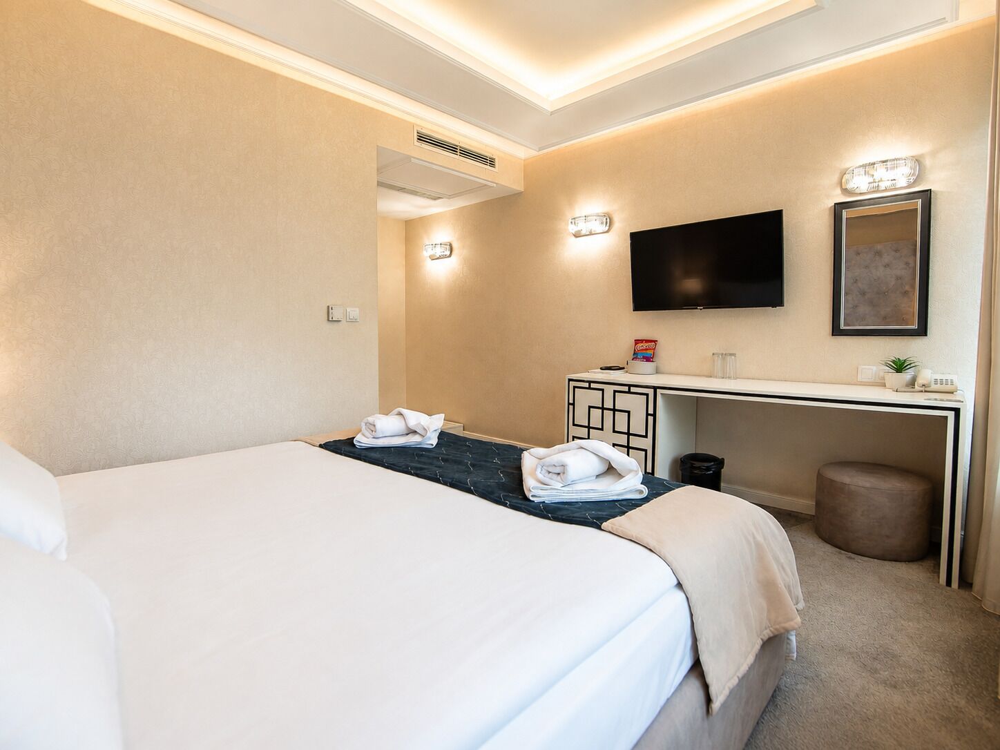 Una habitació d'hotel amb llit, escriptori, televisió i un petit paperer.
