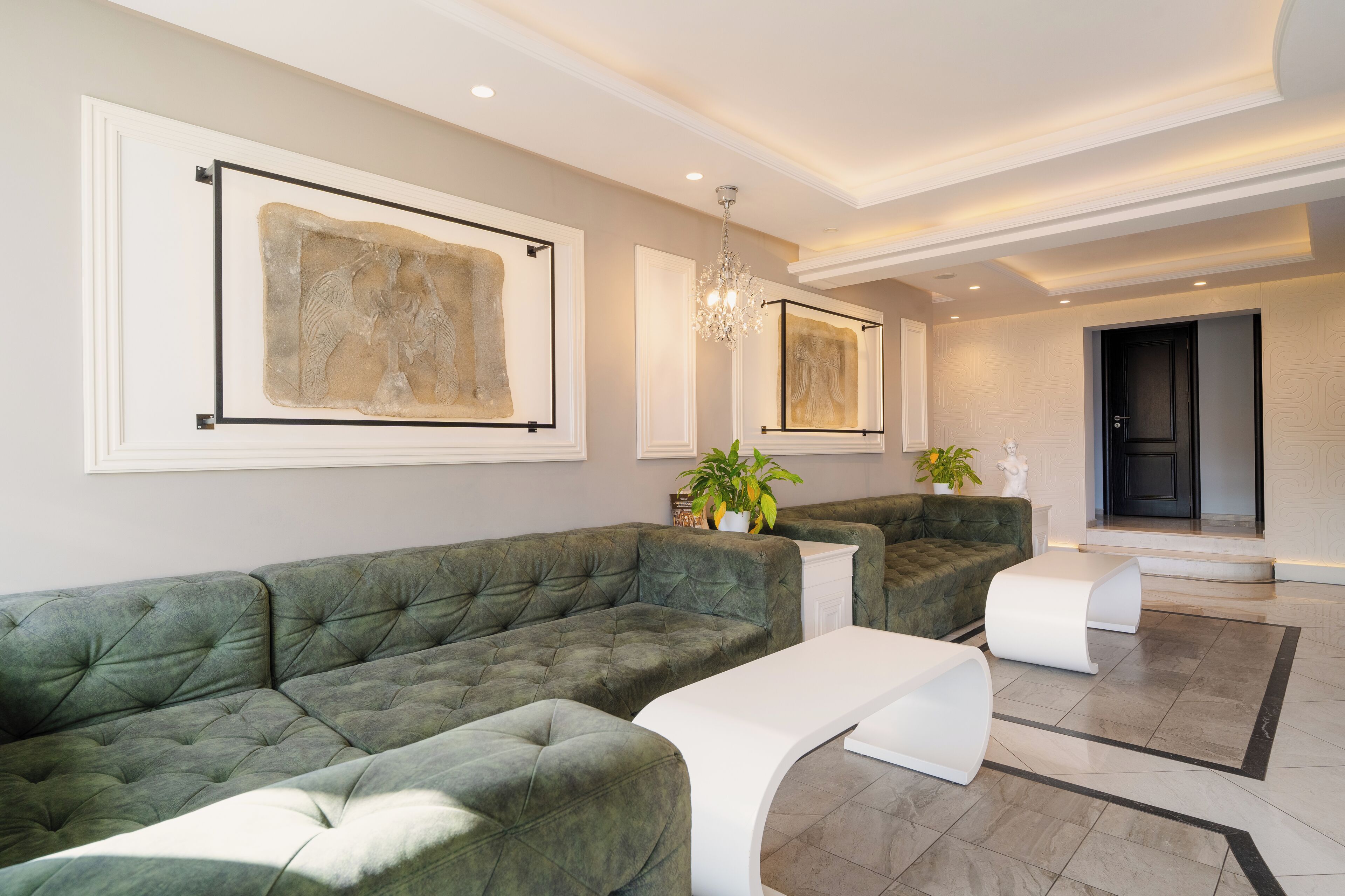 A spacious living area with a green sectional sofa, a white coffee table, and a chandelier.