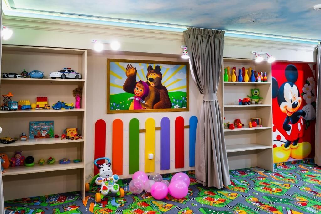 Een kinderspeelruimte met kleurrijke decoraties, een schilderij van een teddybeer en een muurschildering van Mickey Mouse.