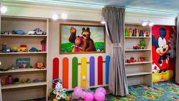 Een kinderspeelruimte met kleurrijke decoraties, een schilderij van een teddybeer en een muurschildering van Mickey Mouse.