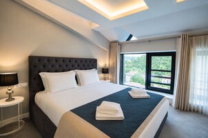 Una habitación de hotel con una cama grande, una mesita de noche, una lámpara y un ventanal con cortinas.