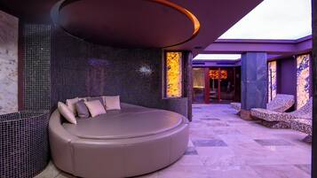 A modern spa room with a circular seating area, a mosaic wall, and a view of the spa entrance.