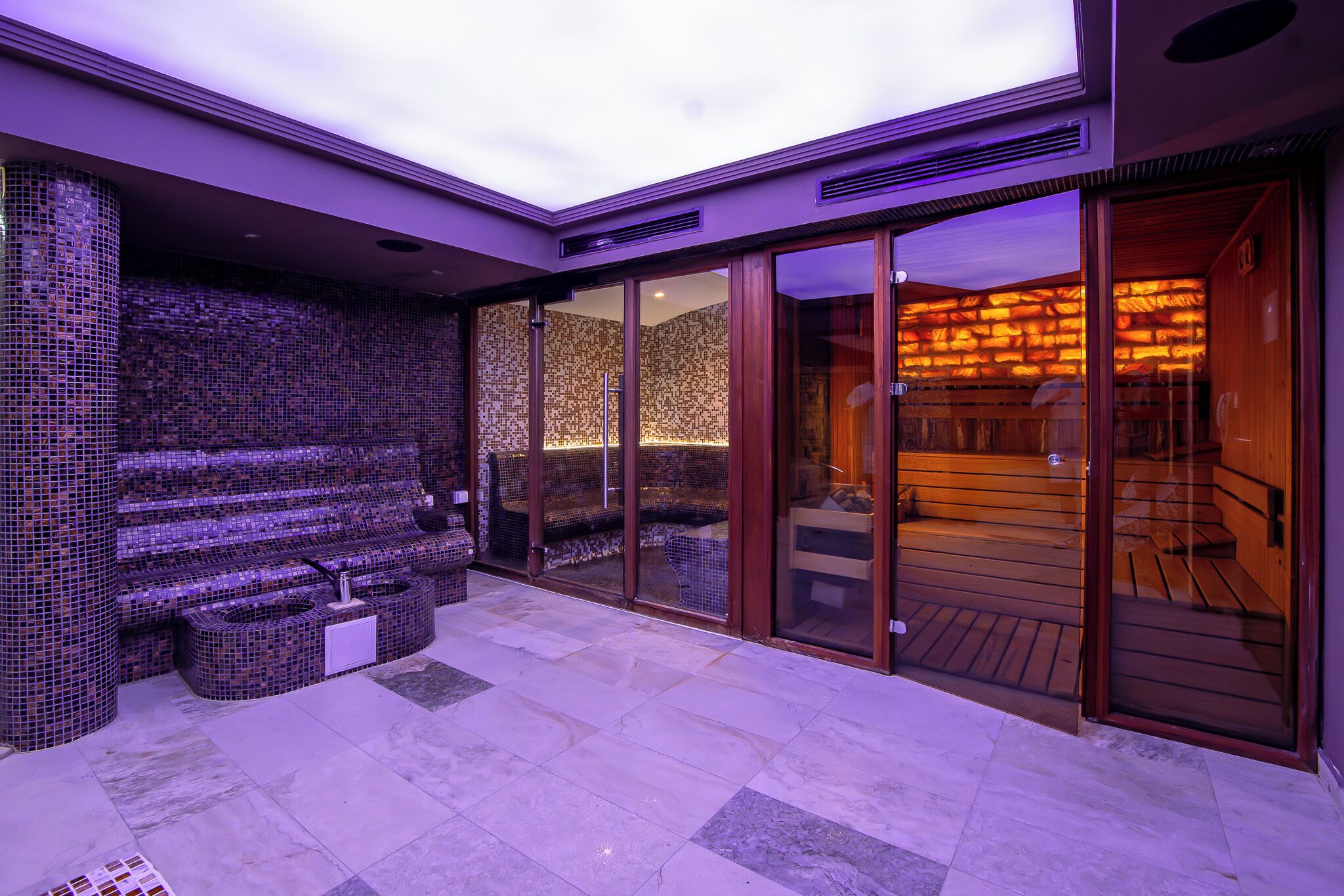 Un'area spa con parete in mosaico, angolo relax e sauna in legno.