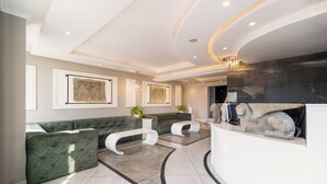 Een moderne lobby met een groene hoekbank, een witte console en een standbeeld van een stenen leeuw.