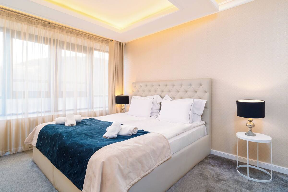 A neatly made bed with a dark blue blanket, a white headboard, and a bedside lamp.