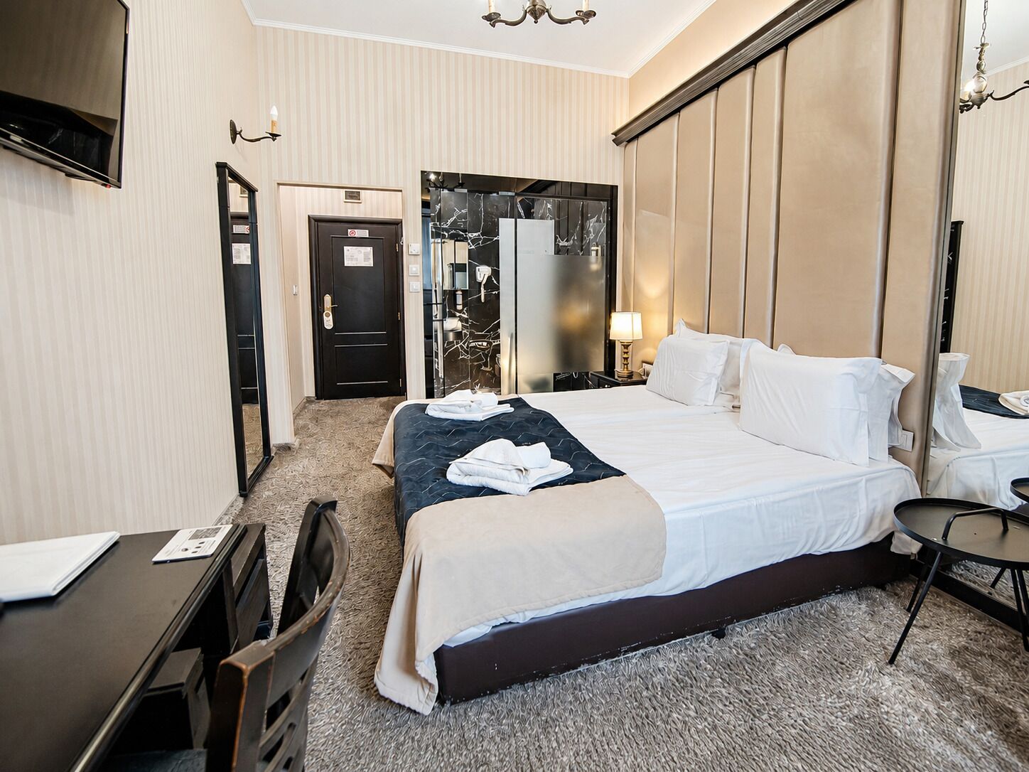 A hotel room with a large bed, a desk, a chair, and a television.