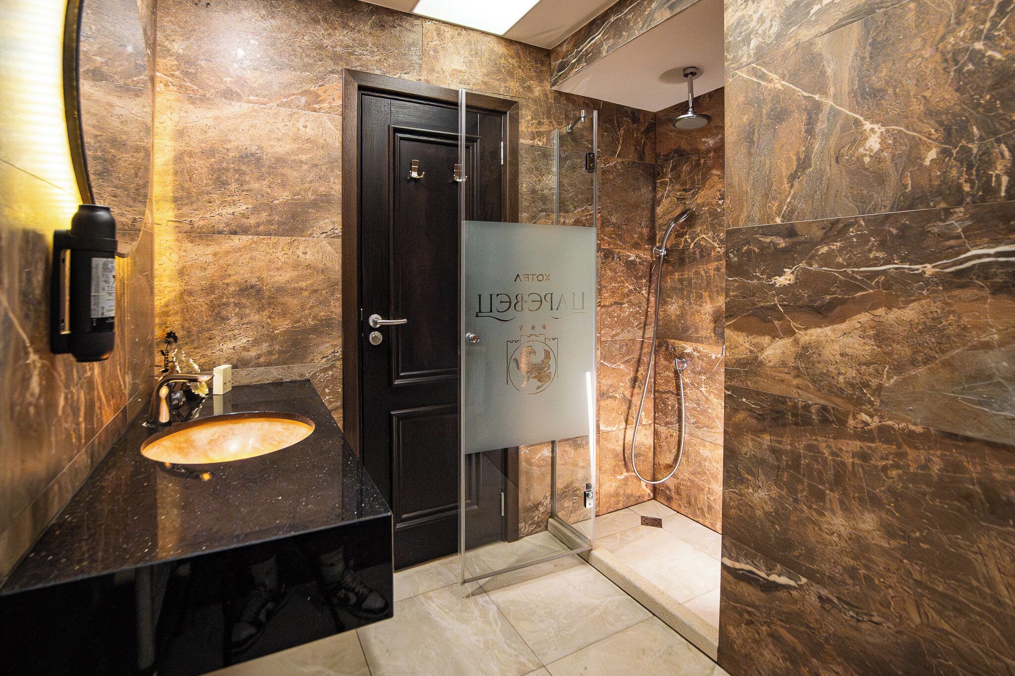 Une salle de bain avec une porte en bois foncé, une douche en verre et un mur recouvert de carreaux de marbre.