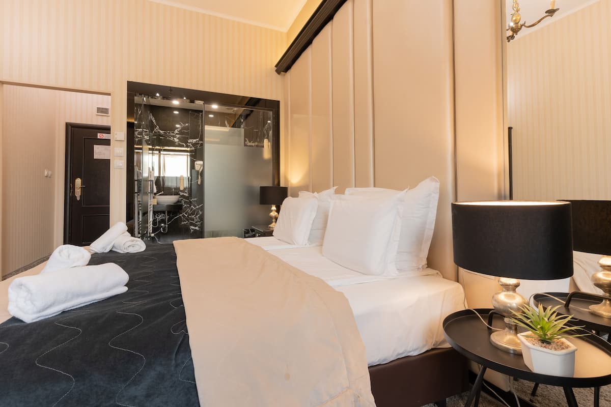 A hotel room with a bed, a bedside table with a lamp, a potted plant, and a mirror.
