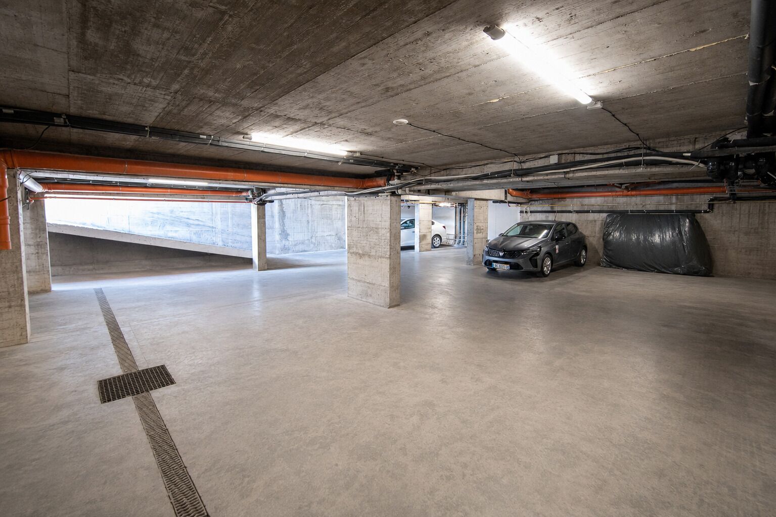Un parking à plusieurs niveaux, avec des piliers en béton, une voiture et un éclairage au plafond.