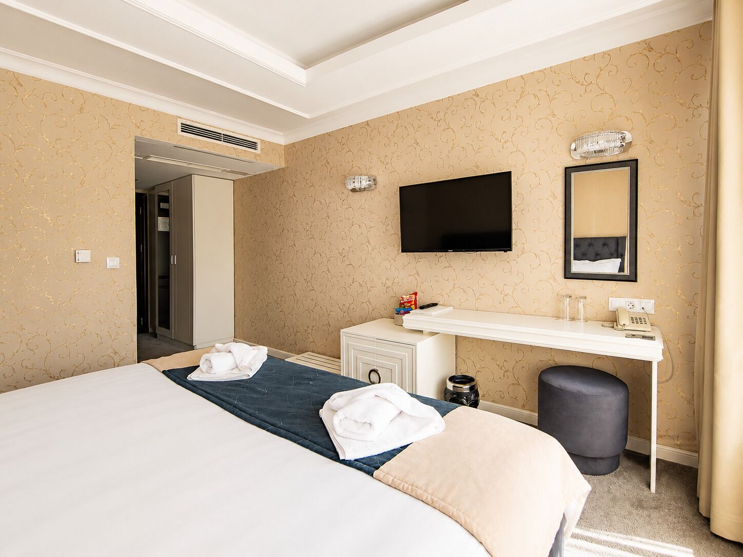 Hotelkamer met een bed, een bureau met een flatscreen televisie, een spiegel en een prullenbak.