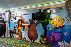 Een kamer met een muurschildering van tekenfilmfiguren, een televisie en een kamerbreed tapijt met een patroon.