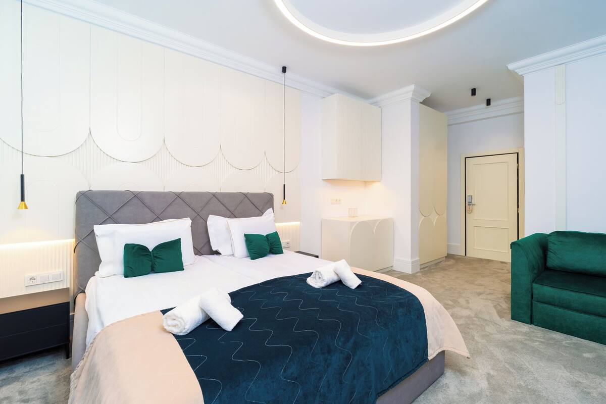 A modern hotel room with a large bed, a green armchair, and a round ceiling light.